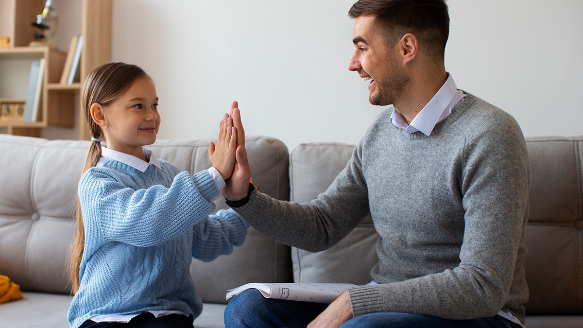 Man and young girl sitting on a sofa, sharing a high-five over a completed worksheet