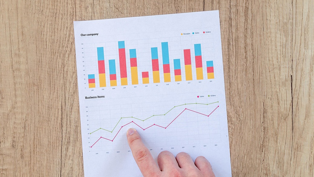 Image of an upward trending report on a desk, with a hand over it point out a detail